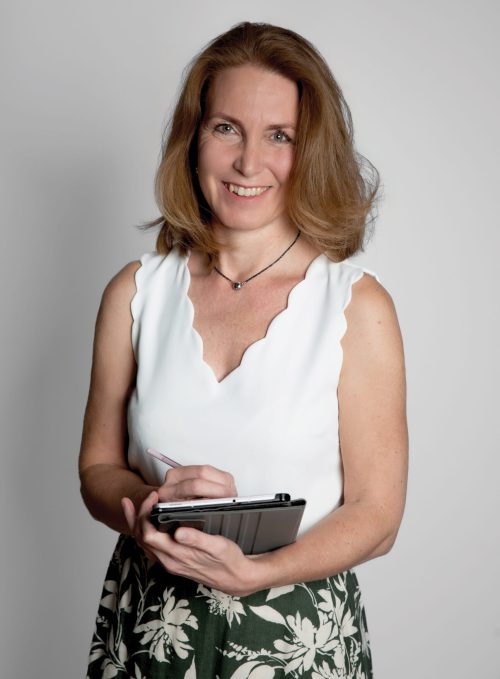 Reichart Anikó egy tabletre jeygzetel, közben a kamerába néz ésmosolyog